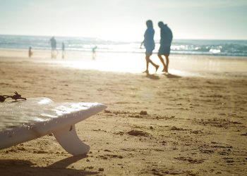 A beach, surfboard, people walking along the beach