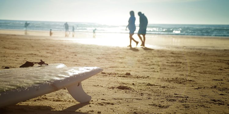 A beach, surfboard, people walking along the beach