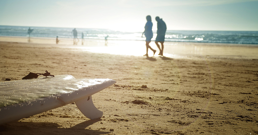 A beach, surfboard, people walking along the beach