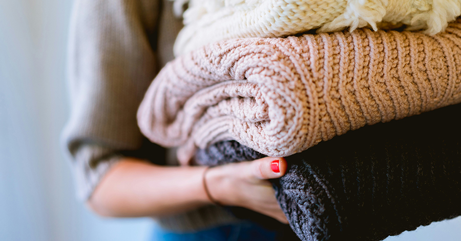 Woman holding a folded pile of sweaters.