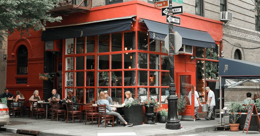 NYC locals dine al fresco at sidewalk tables in New York City’s West Village on a sunny spring day.