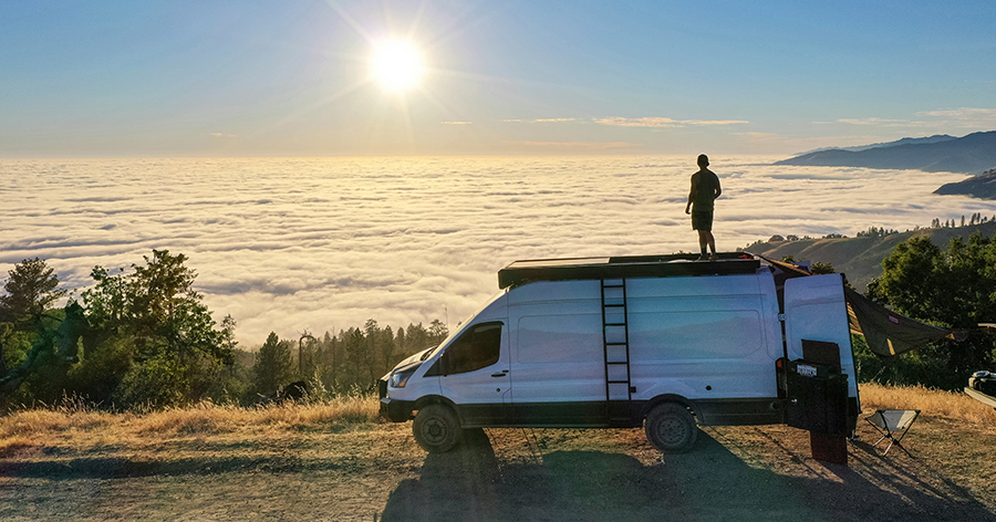 A person standing on top of a van looking at the sun