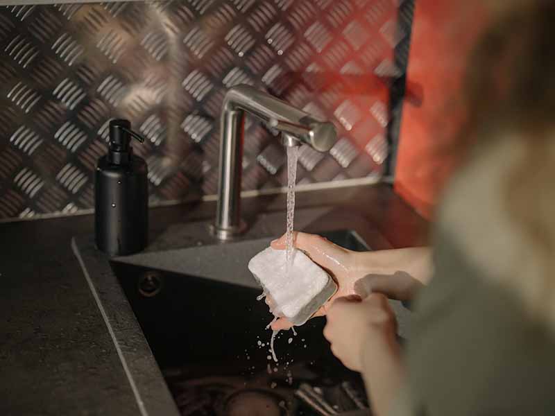 Person cleaning sponge in a sink