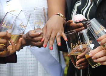 Women holding drinking glasses and looking at a ring on someone's hand