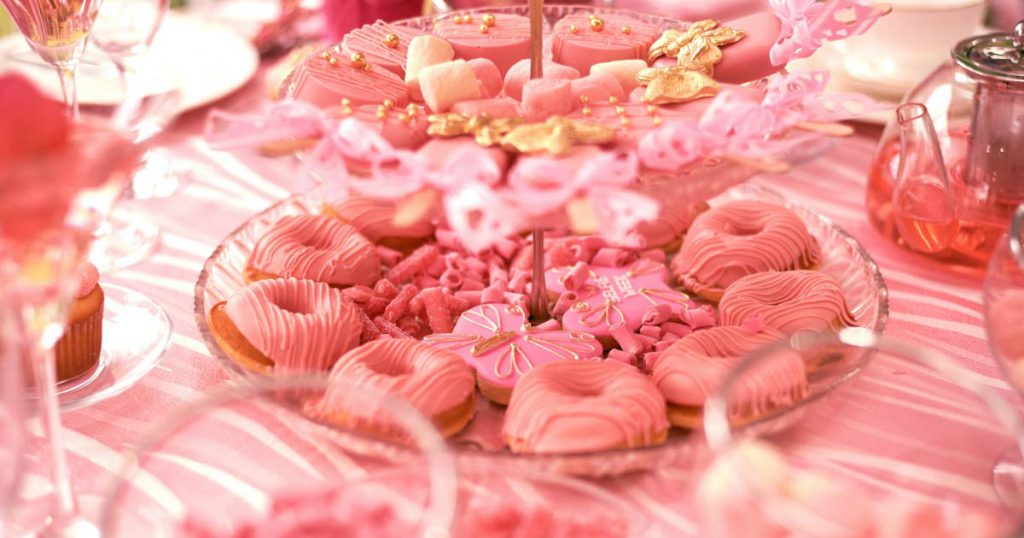 A bridal shower table decorated with a pink cloth and covered in various pink treats, from cookies and marshmallows to floral teas.