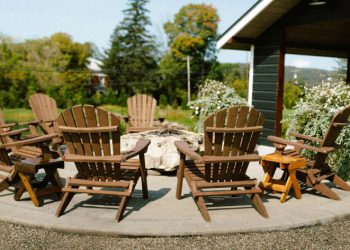 Seven Adirondack chairs are arranged around a stone fire pit on a circular concrete patio.