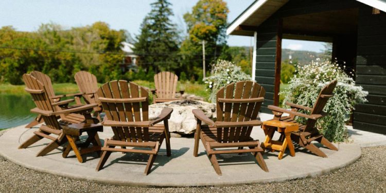 Seven Adirondack chairs are arranged around a stone fire pit on a circular concrete patio.