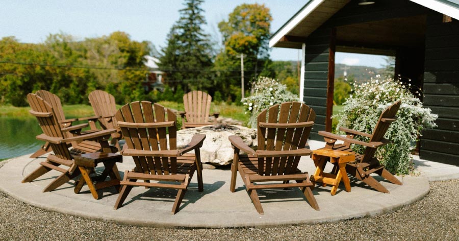 Seven Adirondack chairs are arranged around a stone fire pit on a circular concrete patio.