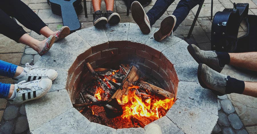 Five friends wearing a variety of shoe styles rest their feet on the edge of a DIY fire pit that was recently added to the patio.