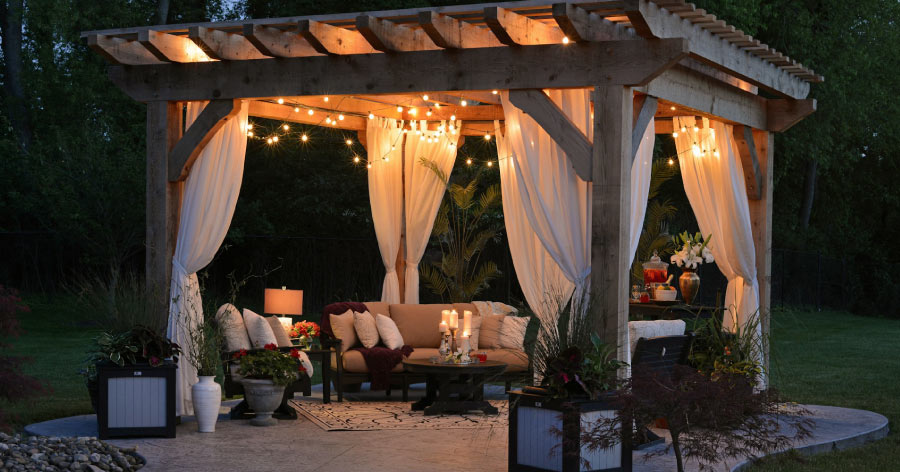 An outdoor patio featuring cozy seating and a pergola decorated with sheer curtains and string lights.