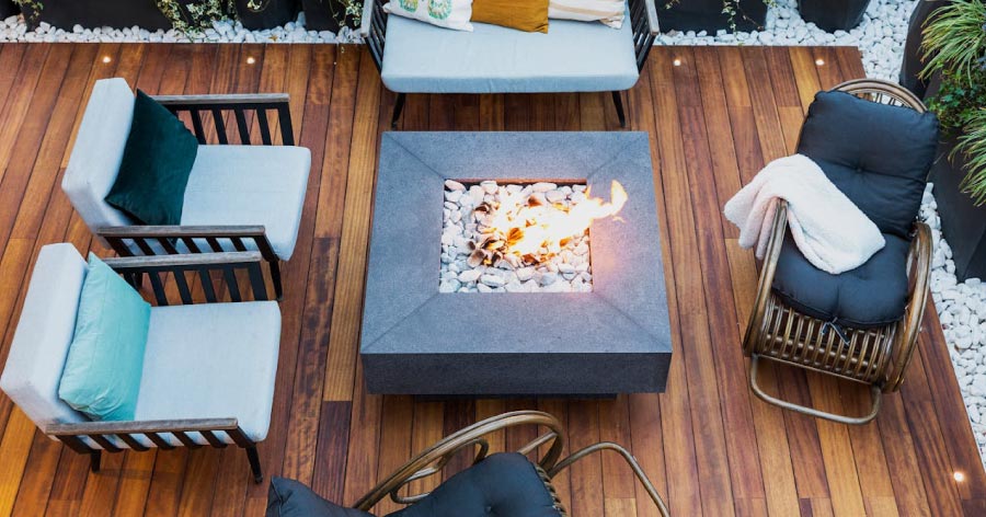 View from above of a newly made-over patio, featuring wicker furniture, a chic fire pit, and a natural wood deck.