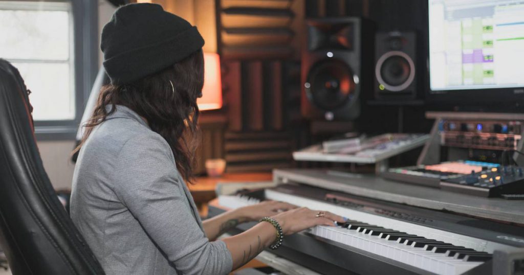 A woman is sitting at her desk, playing keyboard while recording in her home music studio.