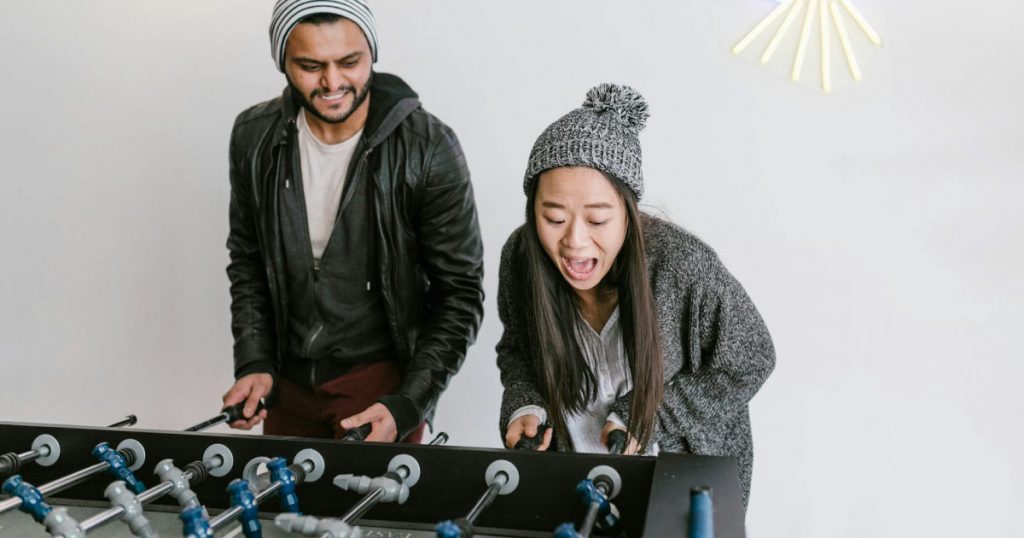 Two friends are enthusiastically playing foosball in a basement game room.