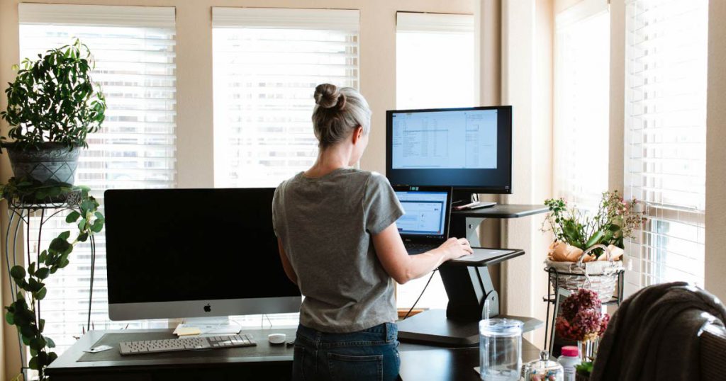A woman is working at a standing desk in a home office she set up in her spare room.