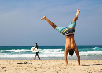 A man in striped board shorts is attempting a handstand on a beach in Fort Lauderdale, Florida.