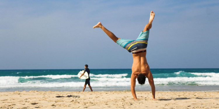 A man in striped board shorts is attempting a handstand on a beach in Fort Lauderdale, Florida.