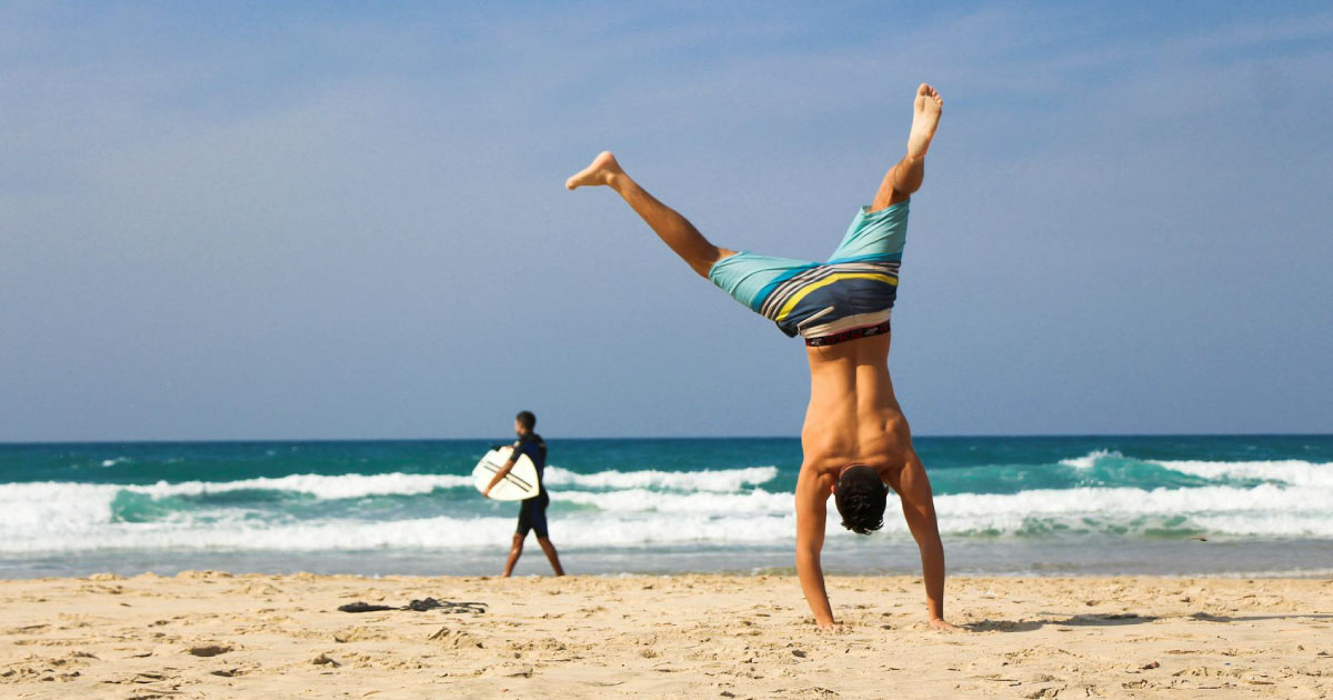 A man in striped board shorts is attempting a handstand on a beach in Fort Lauderdale, Florida.