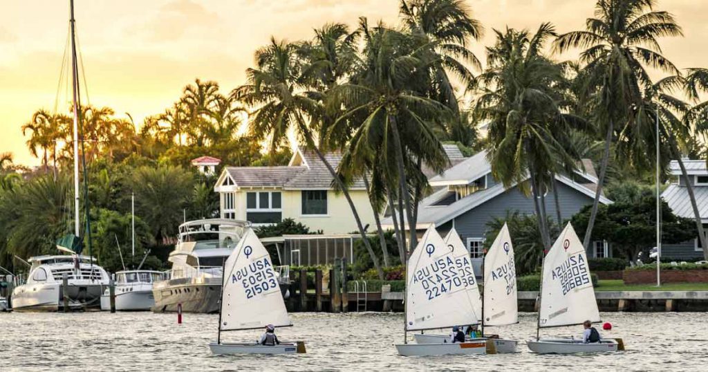 A small group of locals living in Fort Lauderdale sails dinghies past waterfront homes as the sun begins to set.