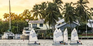 A small group of locals living in Fort Lauderdale sails dinghies past waterfront homes as the sun begins to set.