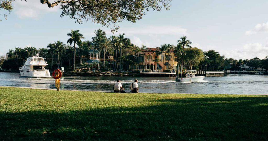 Two men relaxing beside a scenic Fort Lauderdale canal, watching boats as they pass luxury waterfront homes in one of the best neighborhoods in Fort Lauderdale.