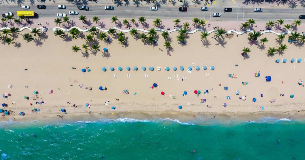 Aerial view of a beach in East Fort Lauderdale, Florida, featuring turquoise waters, creamy sand, and colorful beach umbrellas.