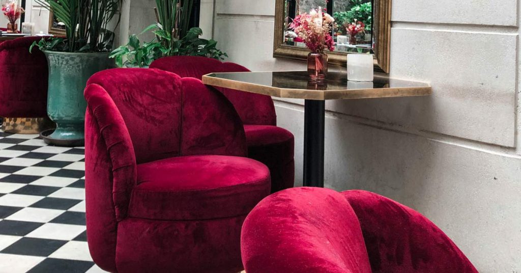 Red velvet chairs are positioned beside café-style tables in a room with checker-patterned tiling on the floor.