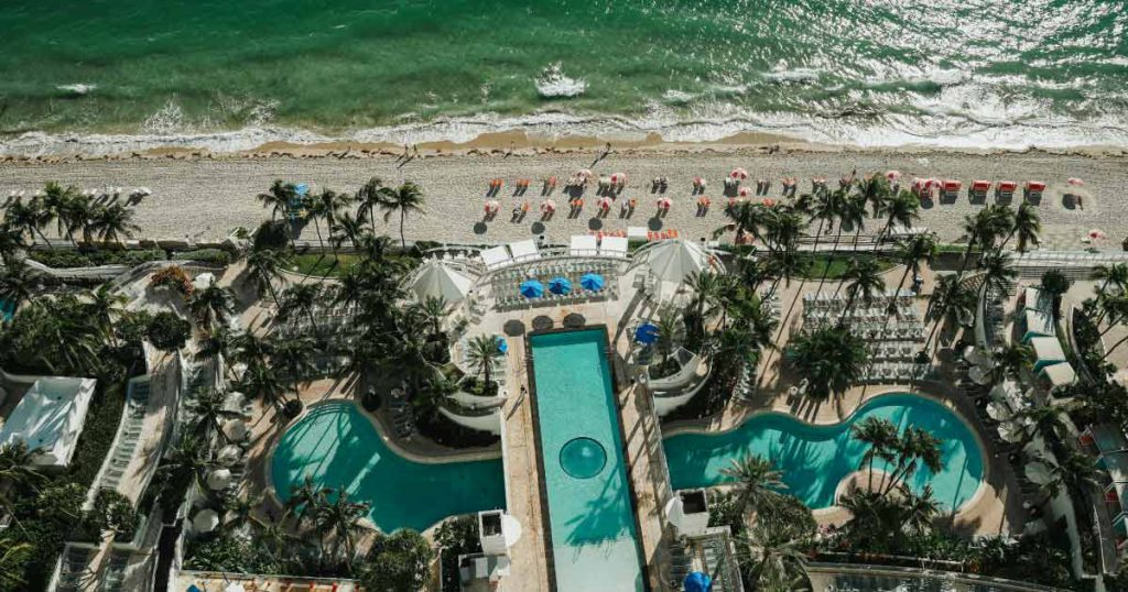 Aerial view of Fort Lauderdale Beach featuring shining surf, palm trees, and an elaborate beachfront resort pool in one of the richest neighborhoods in Fort Lauderdale.