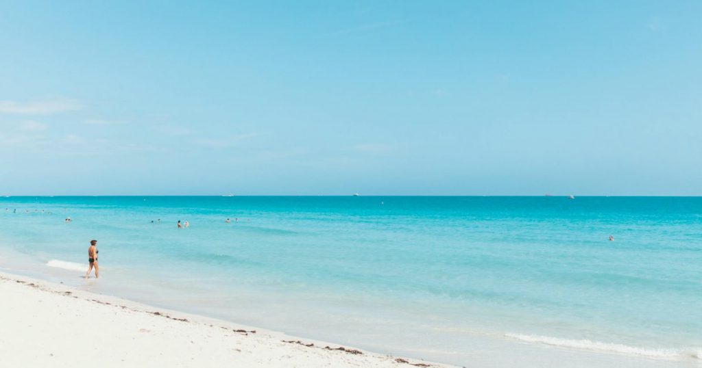 A woman is wading into the blue waters off Fort Lauderdale Beach on a sunny summer day.