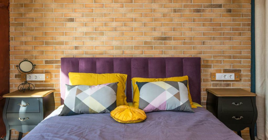 A queen-size bed with an upholstered, plum-colored headboard and colorful accent pillows in yellows, pinks, and grays.