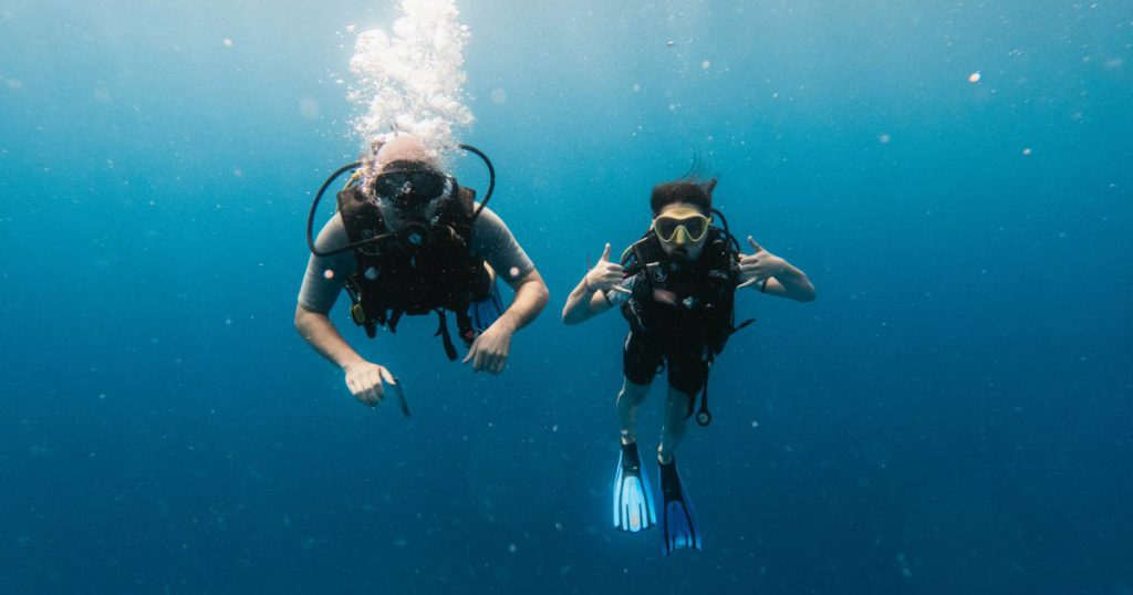 A man and woman are SCUBA diving in blue waters with masks and flippers.