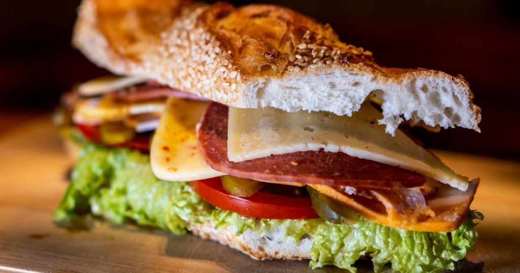Close-up view of a tasty-looking sandwich from one of the best affordable restaurants in Fort Lauderdale, featuring a rustic baguette, premium deli meat and cheese, and fresh veggies.