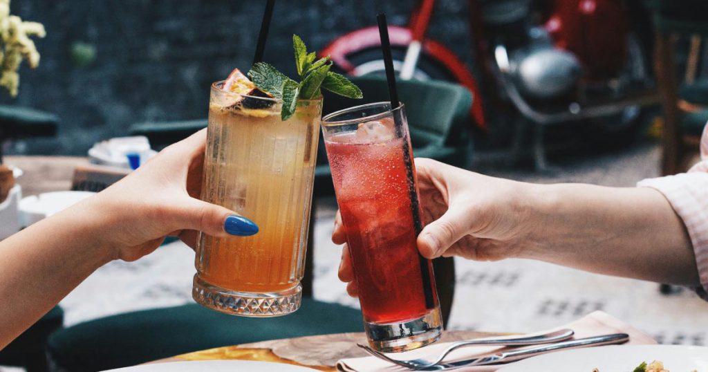 A close-up view of two hands toasting tropical drinks over a table on a sunny day in Florida.