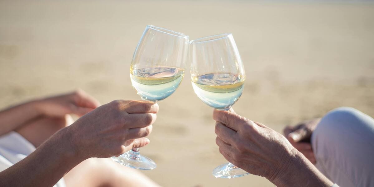 Close-up of a man and woman clinking glasses of white wine together while relaxing on a sunny beach in Fort Lauderdale.