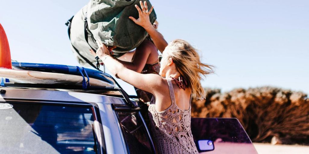 Two women are packing a duffel bag and surfboards on top of a car as they prepare for a day at the beach, one of the perks of living in Fort Lauderdale.