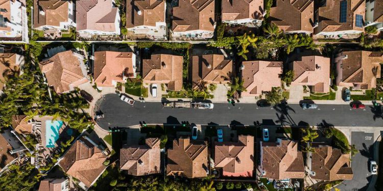 Aerial view of a suburban neighborhood featuring tree-lined streets, a cul-de-sac, and upscale single-family homes with clay-tiled roofs.
