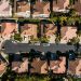 Aerial view of a suburban neighborhood featuring tree-lined streets, a cul-de-sac, and upscale single-family homes with clay-tiled roofs.