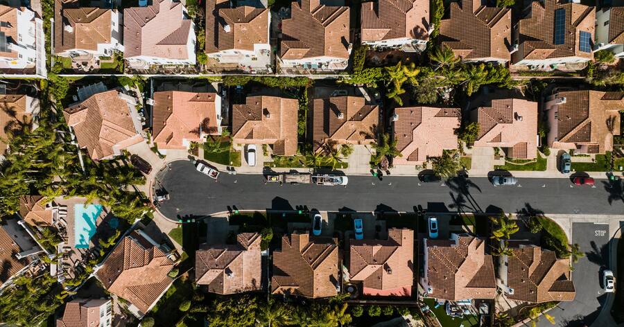 Aerial view of a suburban neighborhood featuring tree-lined streets, a cul-de-sac, and upscale single-family homes with clay-tiled roofs.