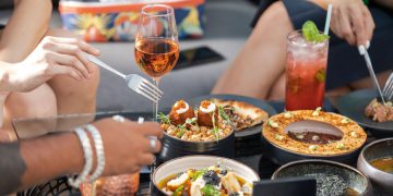 Close-up view of a restaurant table with various upscale dishes and cocktails as friends reach for dishes with their utensils.