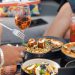 Close-up view of a restaurant table with various upscale dishes and cocktails as friends reach for dishes with their utensils.