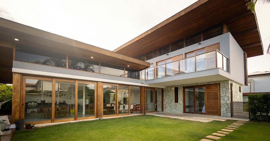 A luxury two-story home with a modern design, featuring wall-to-wall windows, wood accents, and a landscaped backyard.