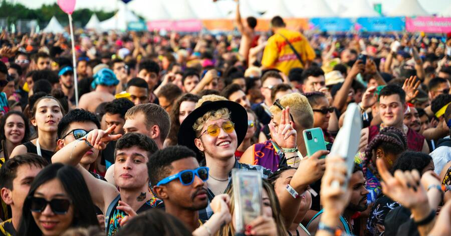 A large, young crowd is enjoying a lively outdoor music festival with people dancing and taking photos.