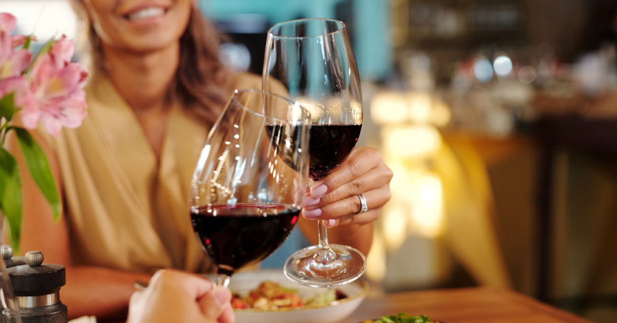 A couple is clinking their wine glasses together over dinner in a warmly lit Las Vegas restaurant.