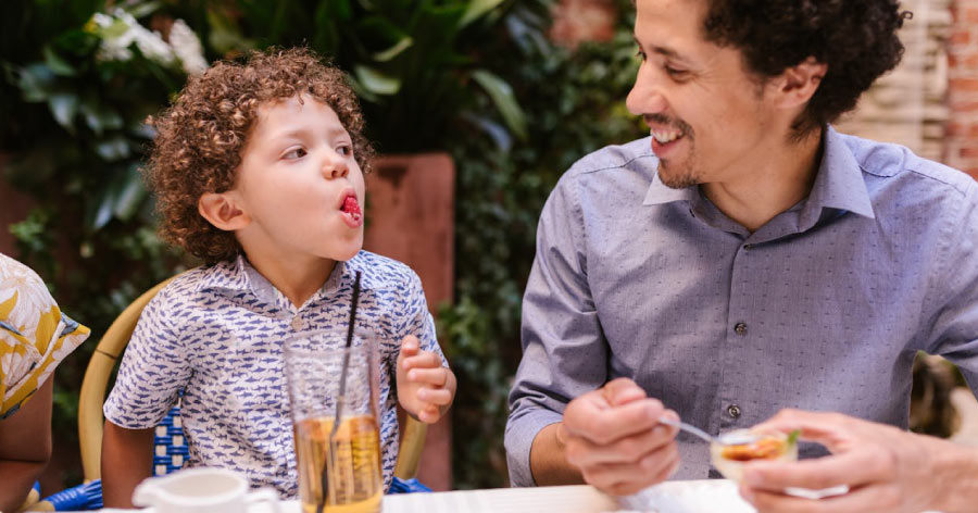 A father smiles at his young son, who is making a funny face while eating a raspberry at a restaurant in Las Vegas.
