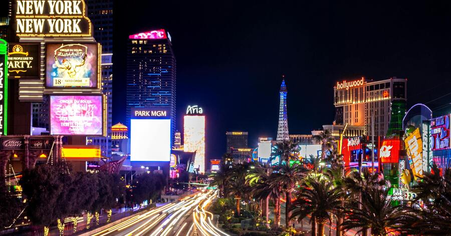 A time-lapsed view of the neon-lit Las Vegas Strip at night, with streaming lights of traffic and iconic hotel signage.