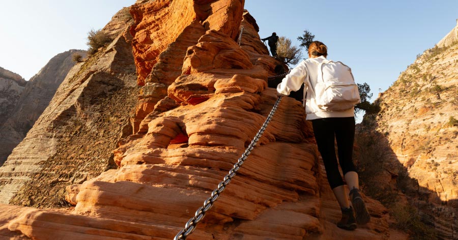 Two hikers are climbing a red rock canyon trail with chain support, showcasing one of the many unique things to do in Las Vegas.