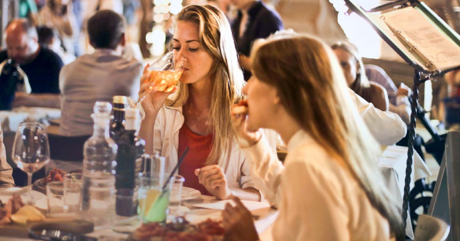 Two women dine together, enjoying wine and a meal in a busy Italian restaurant.