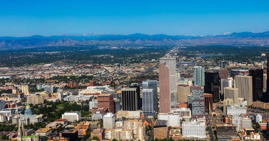Aerial view of Downtown Denver with high-rise buildings, tree-lined streets, and mountains visible in the distance, surrounded by some of the best Denver neighborhoods.
