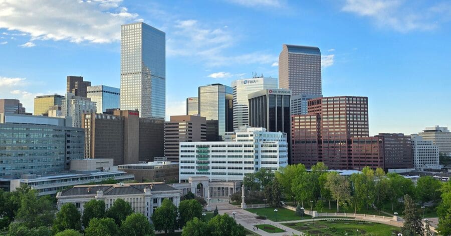 Aerial view of Downtown Denver with high-rise office buildings, a large green park, and dramatic clouds overhead, all common sights when you’re living in Denver.