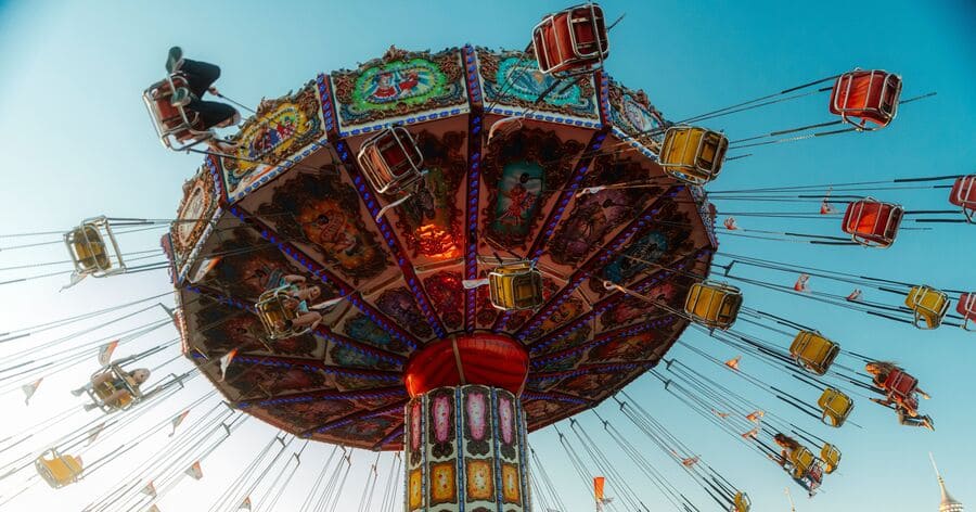 A colorful ride is standing tall above a fairground, spinning riders through the air in suspended swings.