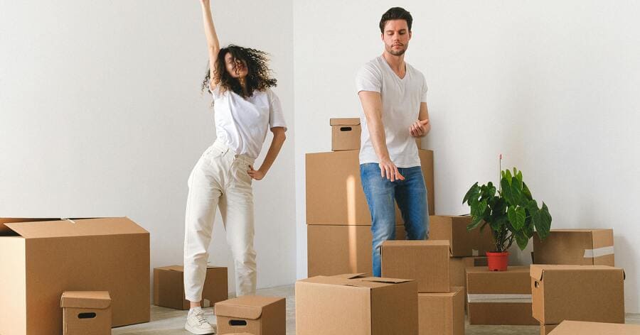 A young couple is standing among moving boxes in a brightly lit home, preparing to unpack after moving to Denver.